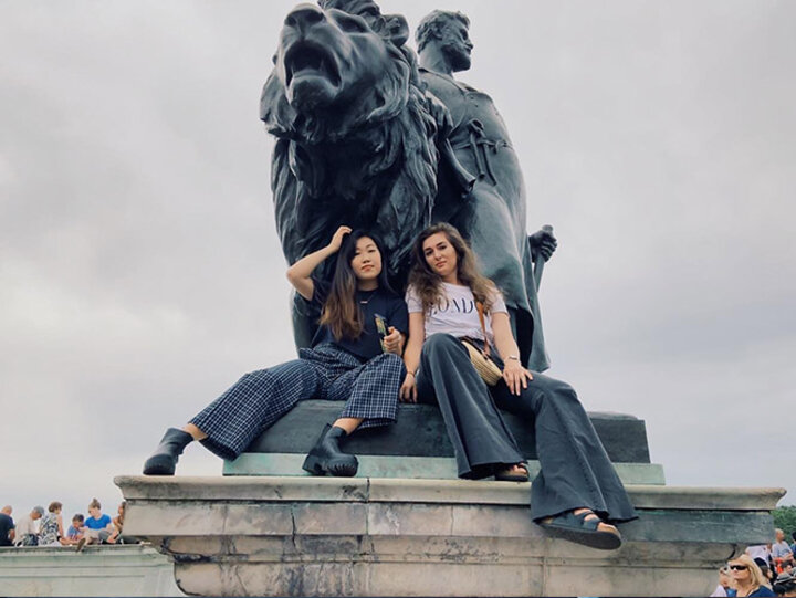 Jessica and Ariel sit with a Victoria Memorial statue before the Changing of the Guards outside Buckingham Palace.